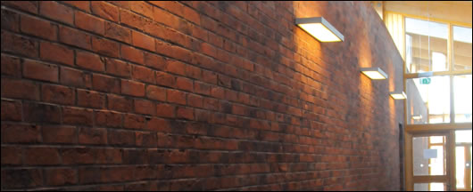 Low energy lighting illuminates the red brick wall which provides linkage and continuity between the three volumes of the building