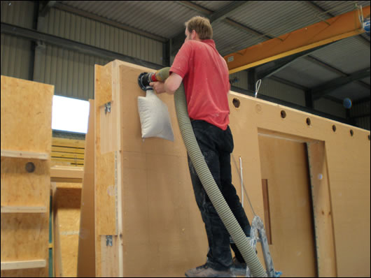 Cellulose insulation pumped into a closed panel wall in a controlled setting