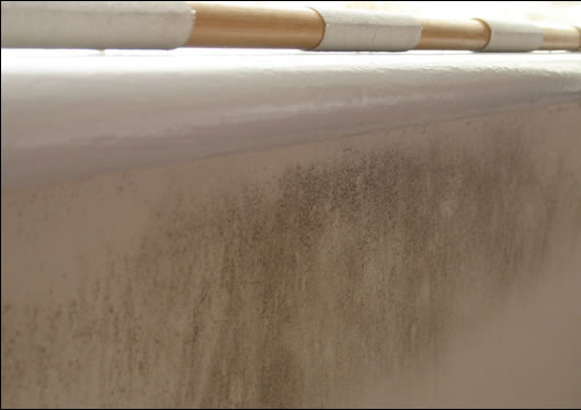 Mould on the south-east facing un-insulated hollow block wall of a bedroom. The dew point moved over a few weeks towards the inside face of the wall in this underheated room which led to mould growth, as furniture or blinds blocked convection currents that would normally evaporate the resulting moisture